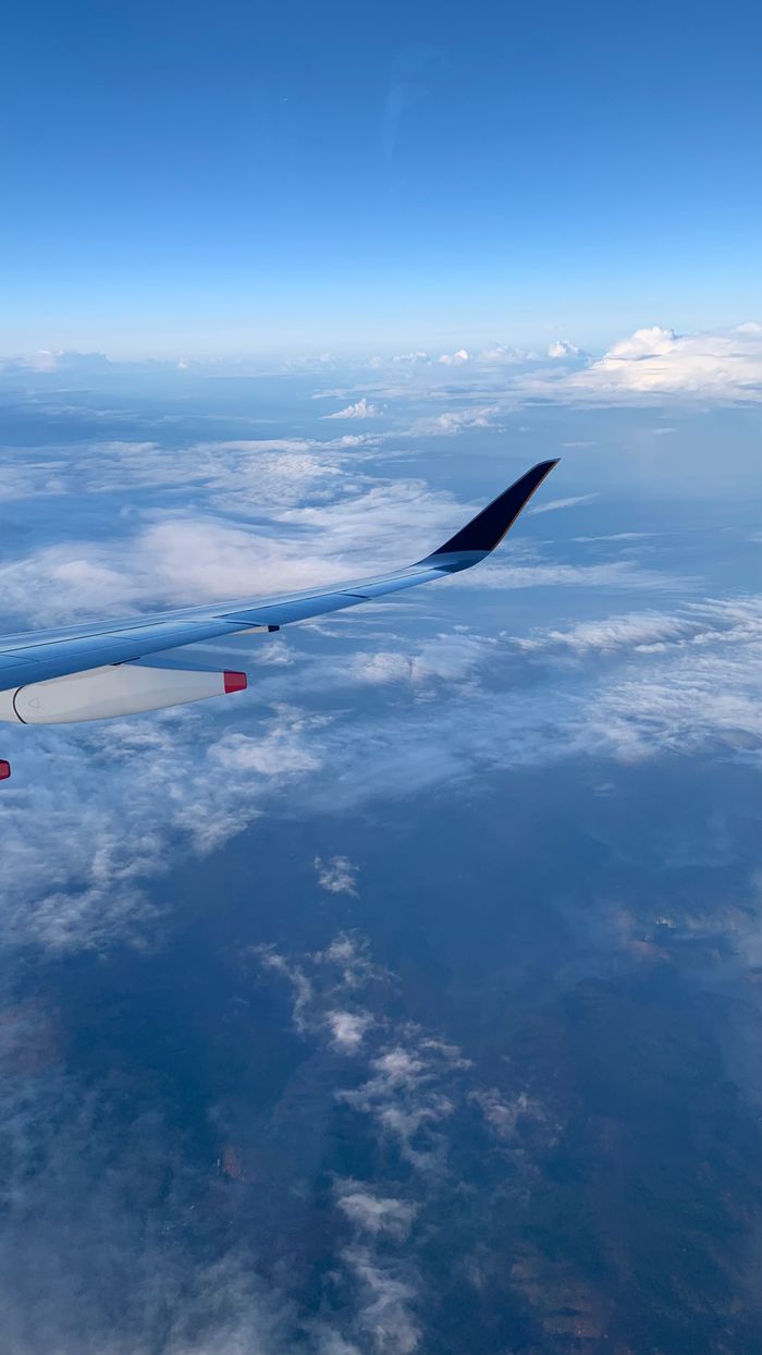 View of clouds and distant land from an airplane, showcasing the beauty of aerial travel.